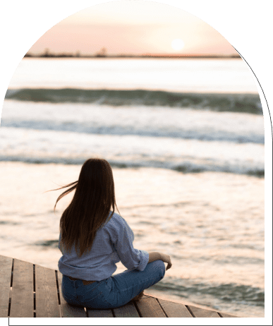 Apprendre à s'organiser apaise l'esprit. Une femme est assise sur le bord de la plage, sereine, et contemple l'horizon.